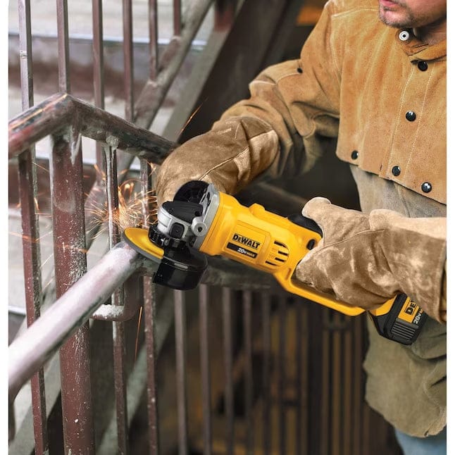 Person wearing protective gear using a DEWALT DCG412B cordless angle grinder to cut a metal railing; sparks flying during active grinding in an industrial setting