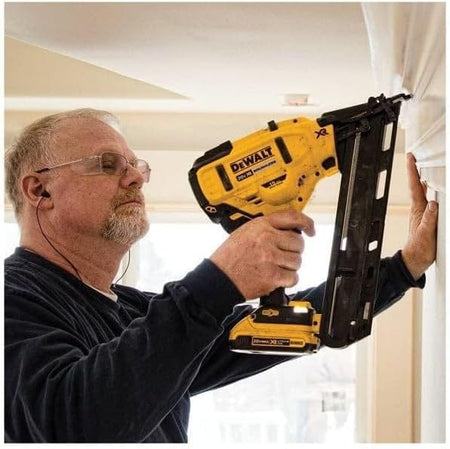 An action shot of a worker using the DeWalt DCN650 15-gauge finish nailer to install white crown molding on a ceiling.