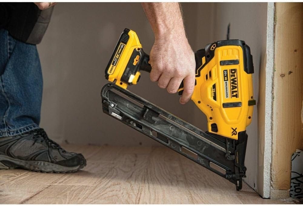 An action shot of a worker in a hard hat using the DeWalt DCN650 cordless finish nailer, with its LED light on, to install white baseboard trim.