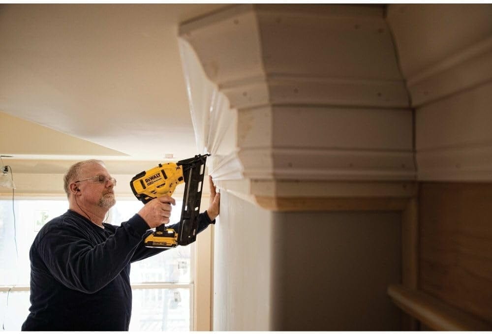 An action shot of a worker using the DeWalt DCN650 finish nailer to install a multi-piece crown molding assembly.