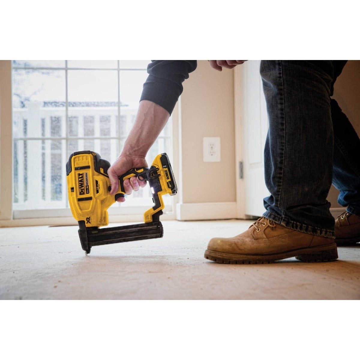 An action shot of a worker using the DeWalt DCN681 cordless stapler, with its LED light on, to fasten flooring underlayment.