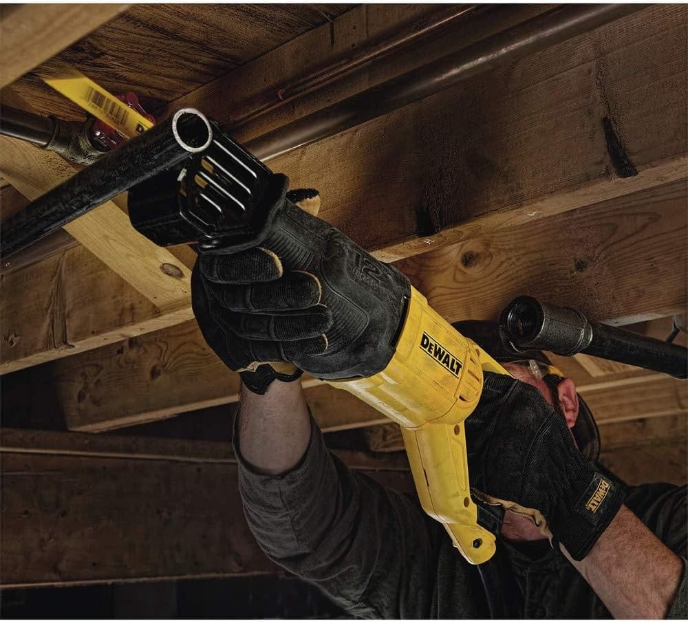 Person using a DEWALT reciprocating saw to cut a metal pipe beneath a wooden structure, wearing gloves and working in a confined construction space