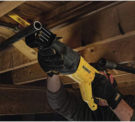 Person using a DEWALT reciprocating saw to cut a metal pipe beneath a wooden structure, wearing gloves and working in a confined construction space