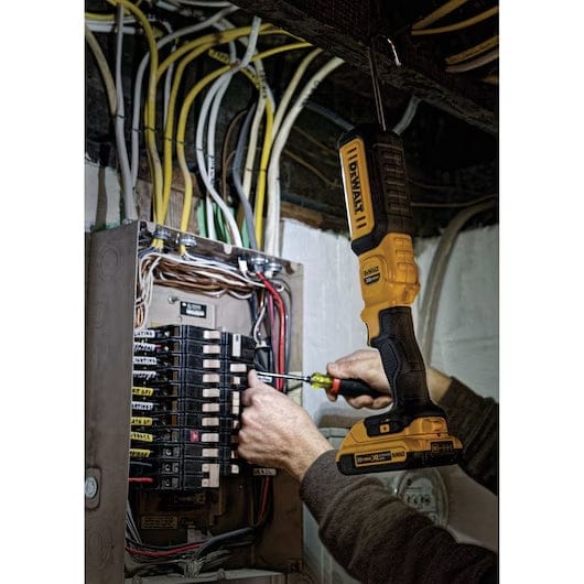 Person working on an electrical breaker panel with a DEWALT reciprocating saw hanging above, showing tool use in electrical maintenance and circuit installation.