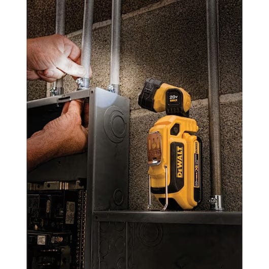 Electrician working on a conduit panel with a DEWALT 20V MAX LED work light positioned nearby, illuminating the workspace in an industrial setting.