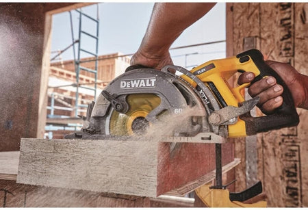 Close-up of a DEWALT cordless circular saw actively cutting wood at a construction site, with sawdust flying and framing materials in the background