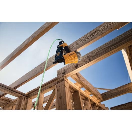 DEWALT pneumatic nail gun connected to green air hose, positioned against a wooden beam at a construction site with clear blue sky in background.