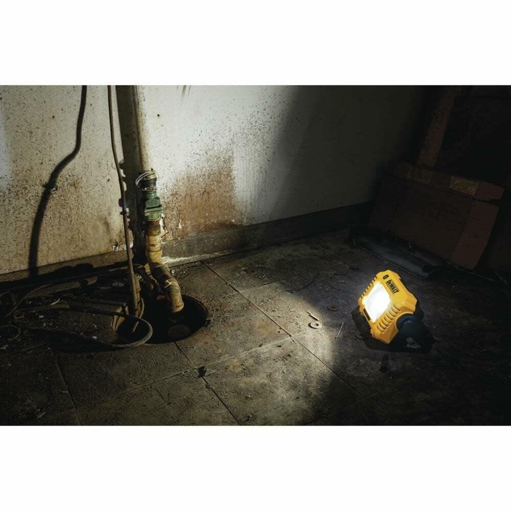 The DEWALT compact LED work light sits on the floor of a dark basement, casting a bright beam of light across the room.