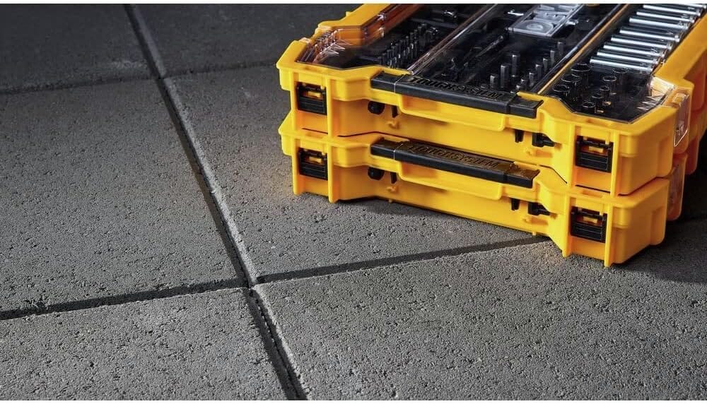 Stacked DEWALT ToughSystem 2.0 tool trays resting on a concrete floor, highlighting the side latches used for modular connection and secure transport on the jobsite.