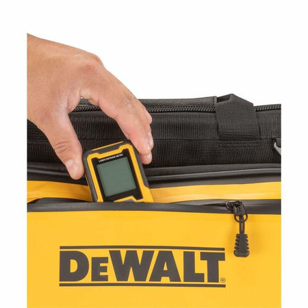 A close-up view of a hand placing a DEWALT laser distance meter into the front pocket of the tool bag.