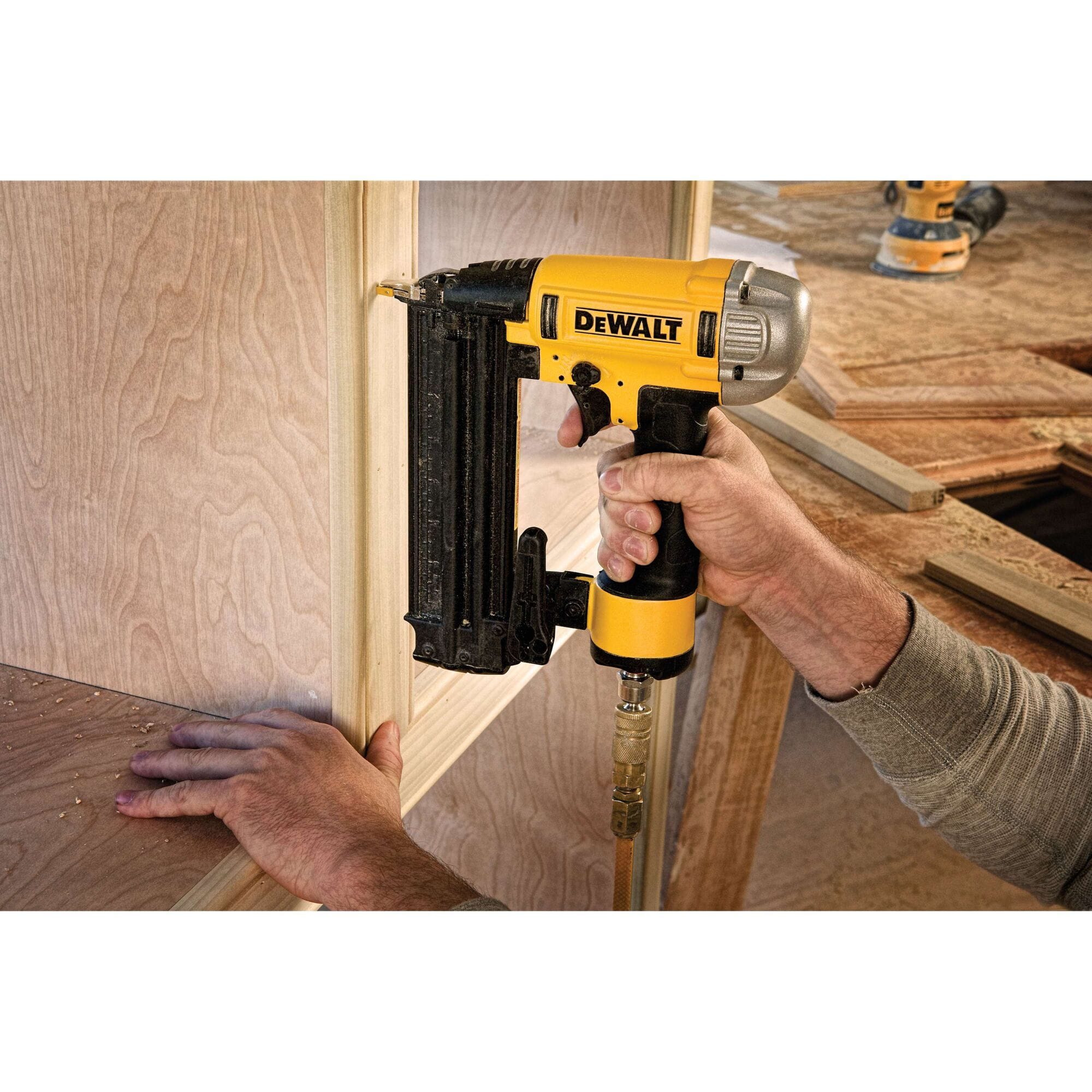 A carpenter using the DEWALT 18 GA pneumatic finish nailer to install decorative wood trim on a cabinet, showcasing the tool's compact size and maneuverability in tight corners.