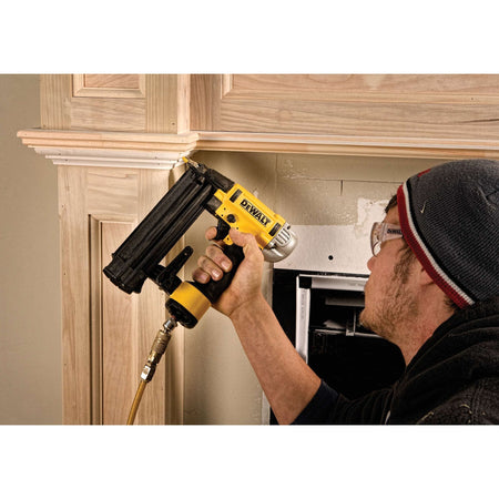 DEWALT DWFP12233 brad nailer being used by a professional to secure crown molding to a fireplace mantel, highlighting the selectable trigger for precise sequential firing.