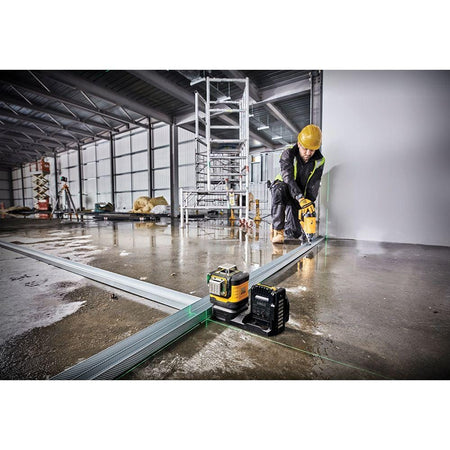 DEWALT DCLE34520G green beam laser level placed on a concrete floor to project long horizontal and vertical lines for aligning metal track during framing.