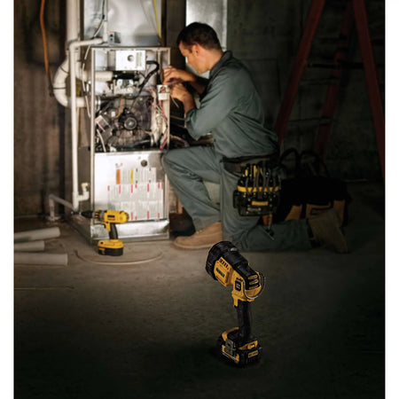 An action lifestyle shot showing the DEWALT spotlight providing hands-free area lighting for an HVAC technician. The light is standing on the floor, tilted upward to illuminate the interior of a furnace unit during a repair.