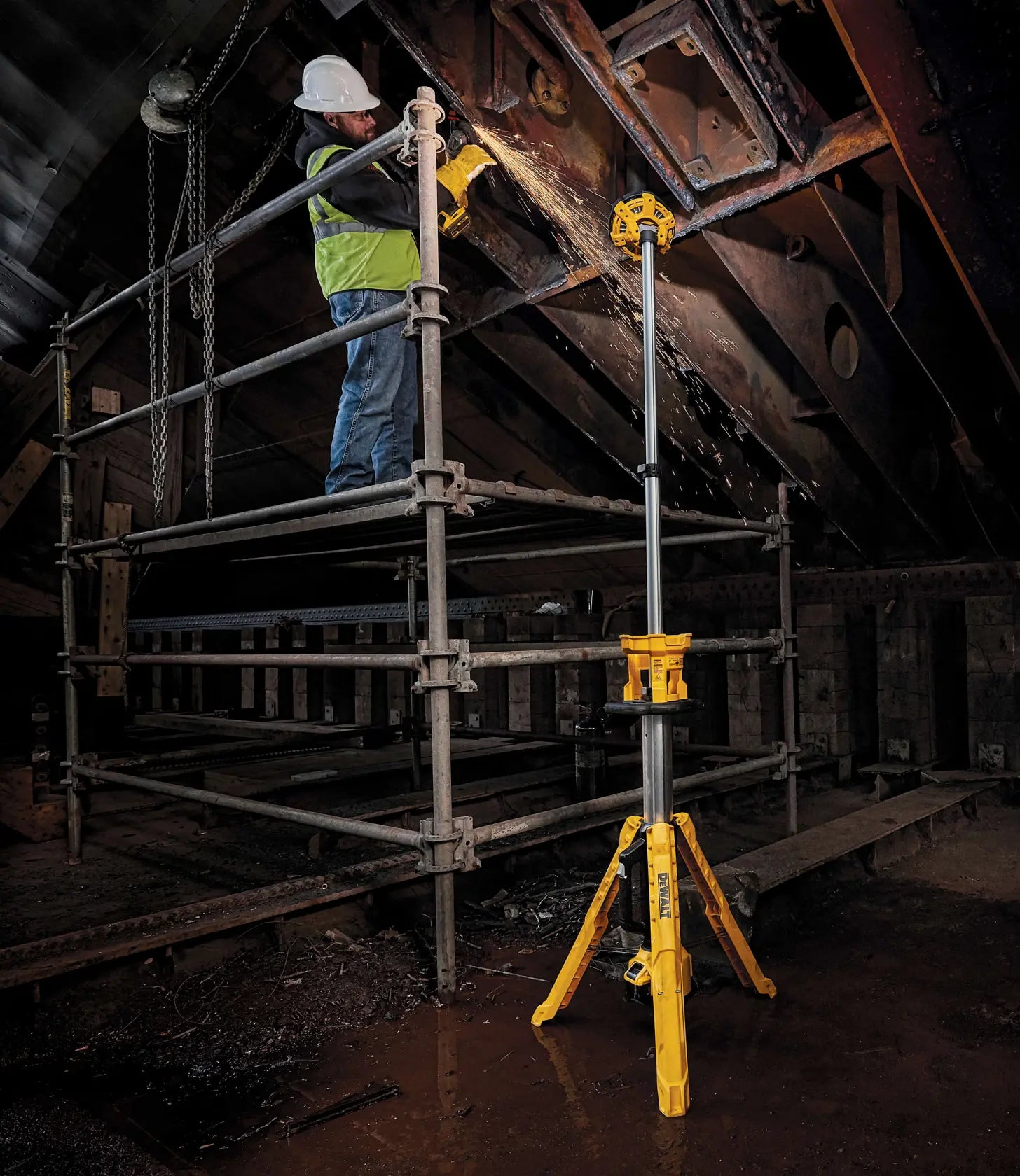 A lifestyle shot of the DEWALT telescoping light extended to its full 7-foot height. The light is being used to provide overhead illumination for a contractor working on high scaffolding, showcasing the reach and versatility of the adjustable light head.