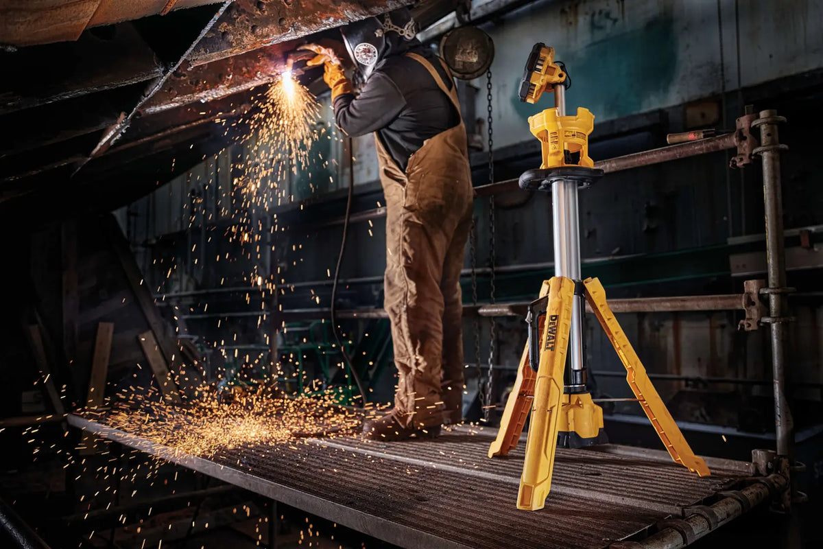 An action lifestyle shot from a low angle, showing the DEWALT DCL079B lighting up a dark jobsite. The pivoting head is directed toward a work surface where sparks are flying, demonstrating the tool's impact-resistant shroud and industrial-grade durability.