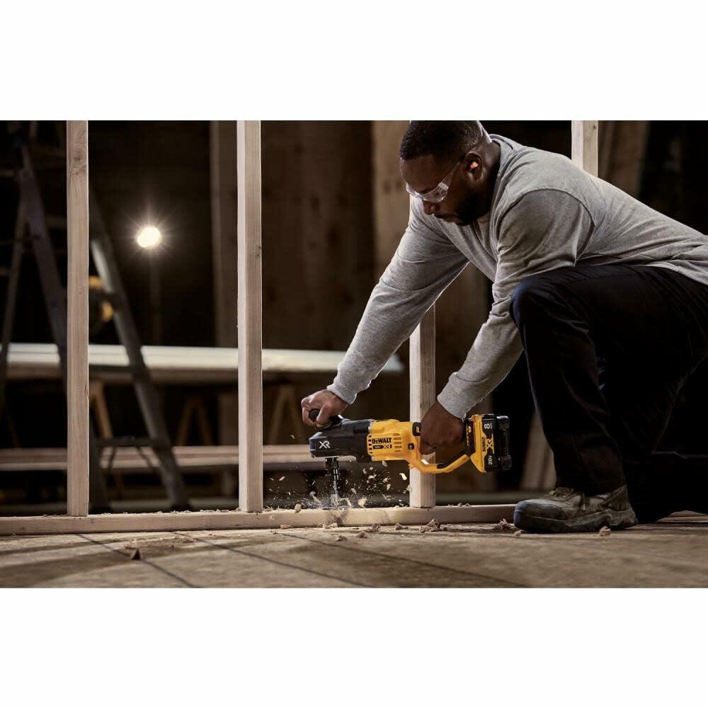 A worker on a construction site kneels to use the DEWALT Stud and Joist Drill to power through a thick wooden joist on the floor.