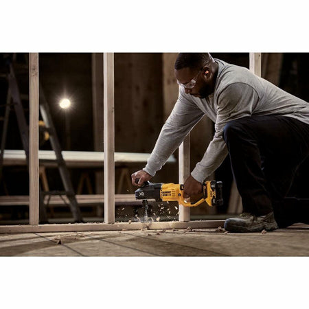 A worker on a construction site kneels to use the DEWALT Stud and Joist Drill to power through a thick wooden joist on the floor.
