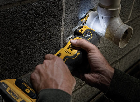Person using a DeWalt power tool on a pipe against a textured wall.