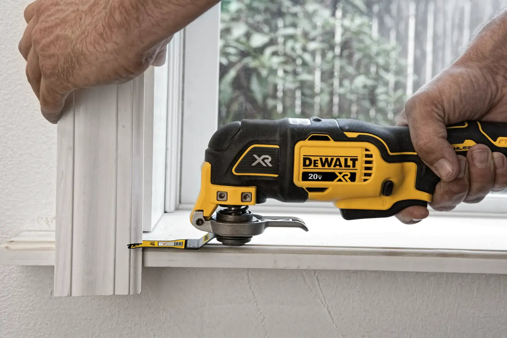 DEWALT 20V MAX XR Brushless Oscillating Multi‑Tool DCS356 trimming wooden molding near a window frame, demonstrating accurate detail cutting for carpentry and home improvement projects.