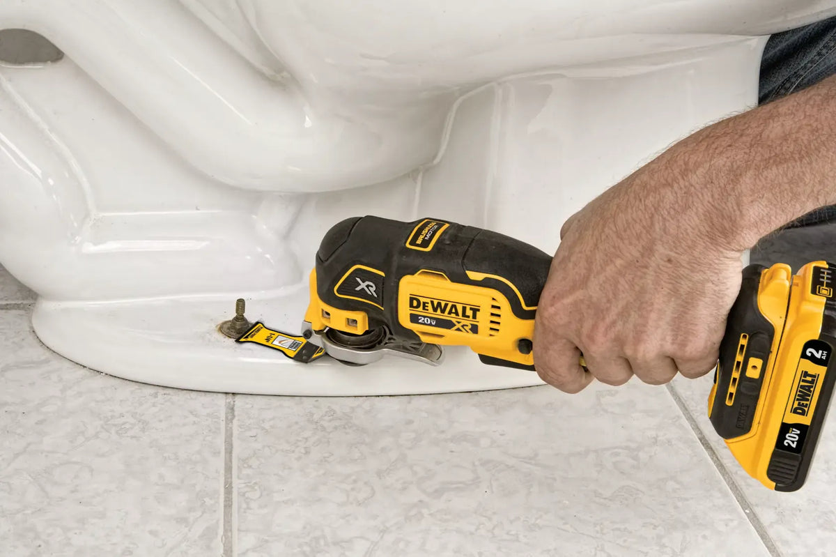 Alt text: Close‑up of a DEWALT 20V MAX XR Brushless Oscillating Multi‑Tool DCS356 being used to cut a toilet bolt cap at the base of a toilet, showing precise cutting capability and ergonomic control for plumbing and home repair tasks.