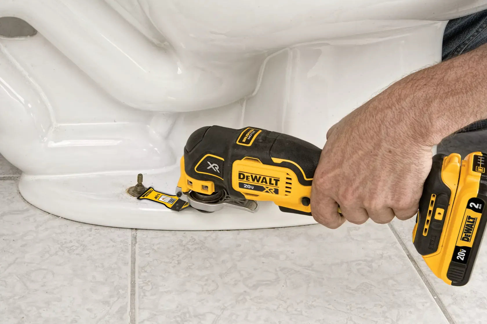 Alt text: Close‑up of a DEWALT 20V MAX XR Brushless Oscillating Multi‑Tool DCS356 being used to cut a toilet bolt cap at the base of a toilet, showing precise cutting capability and ergonomic control for plumbing and home repair tasks.