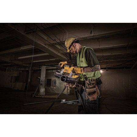 An action lifestyle shot of a professional contractor using the DEWALT 20V MAX XR brushless band saw to cut through large-diameter steel pipe secured on a tripod vice. The image demonstrates the tool's 5-inch deep cut capacity and cordless efficiency in a construction jobsite setting.