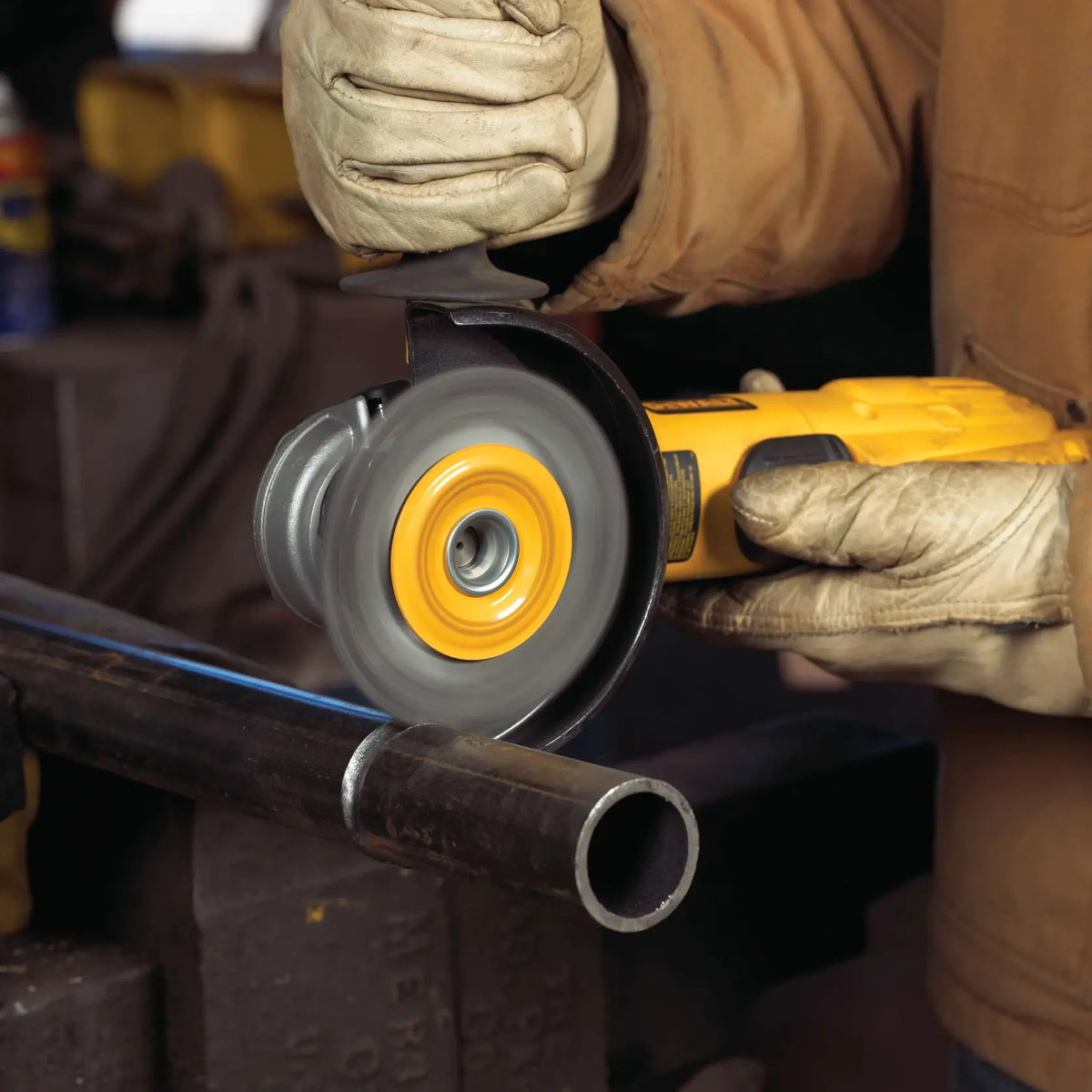 A lifestyle image of a worker using the DEWALT DW4925B wire wheel on a corded angle grinder. The spinning wire brush is shown cleaning a circular weld on a metal pipe, highlighting the tool's precision in narrow weld cleaning applications.