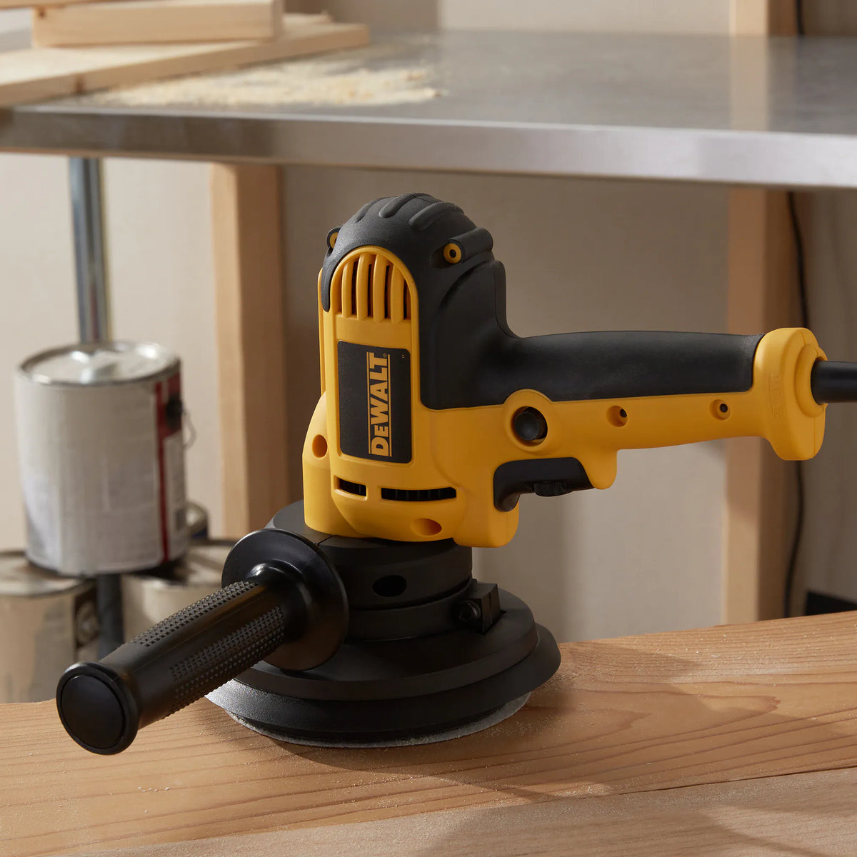 The DEWALT 6-Amp corded rotary sander DWE6401DS resting on a finished wood surface, highlighting the mid-handle design and adjustable dust shroud for professional woodworking.