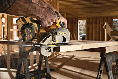 An action lifestyle shot from behind the tool, showing a carpenter making a precision crosscut in framing lumber. The image highlights the ergonomic top handle grip and the high-capacity 9.0Ah FLEXVOLT battery providing consistent power through a heavy-duty wood cut.