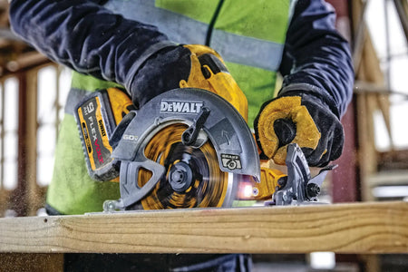 A close-up action shot of the DEWALT 60V circular saw in operation. The image showcases the bright LED work light illuminating the cut path and the integrated electronic brake logo on the blade guard, emphasizing safety and visibility during professional use.