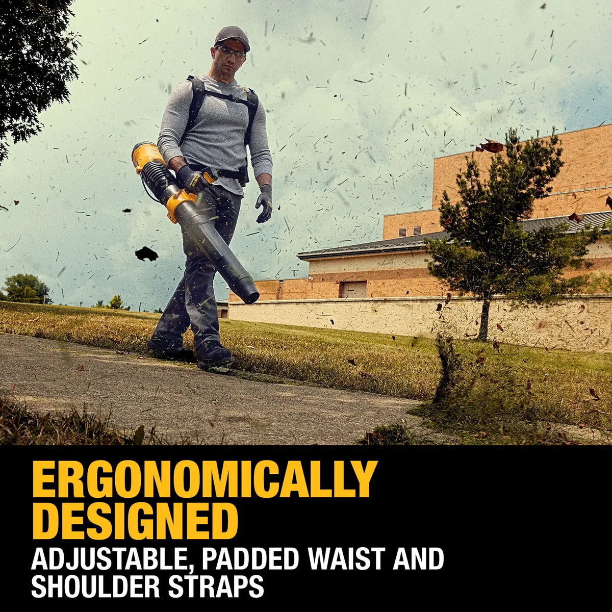 Worker using the DEWALT 60V MAX FLEXVOLT Brushless Backpack Blower DCBL570Z2 with padded waist and shoulder straps while clearing leaves along a sidewalk, emphasizing ergonomic design for long‑duration use.