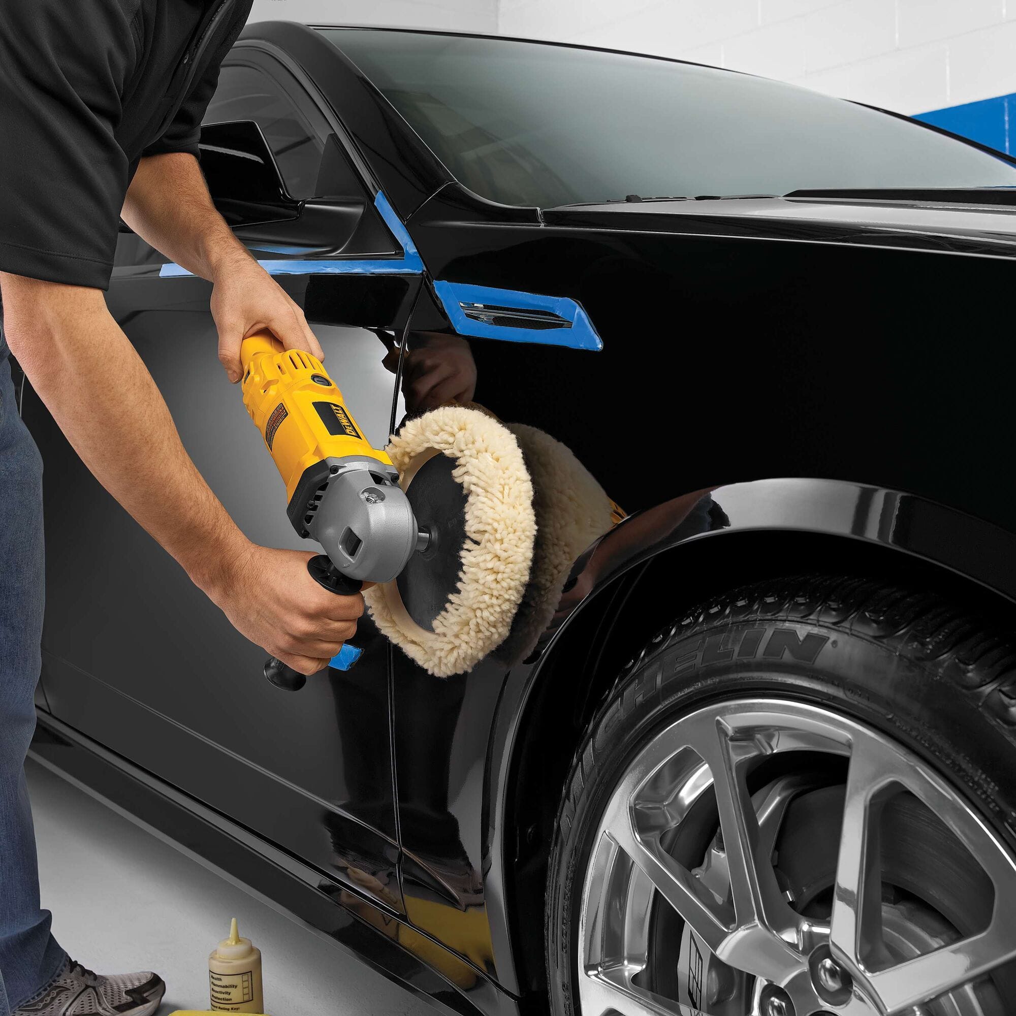 A detailer using the DEWALT DWP849 12-Amp motor corded polisher and a wool buffing pad on a black vehicle fender, demonstrating the precision control required for automotive detailing and finishing.