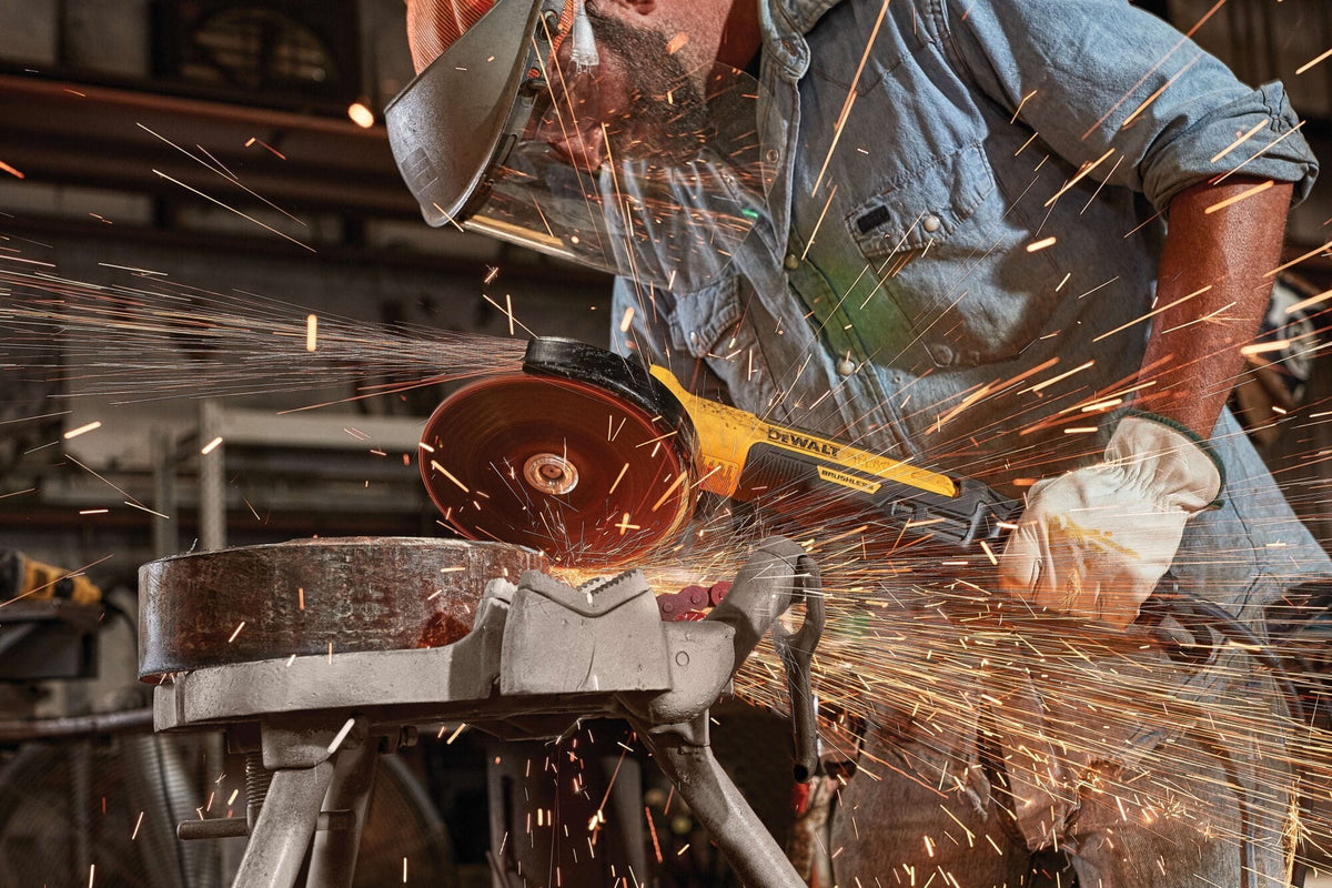 Extreme close-up view of a DEWALT corded angle grinder cutting through a thick structural steel component, creating a bright stream of sparks, showing the tool's yellow housing and protective metal wheel guard layout.