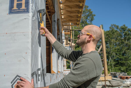 Action shot of a professional installer using the DEWALT lightweight composite hammer tacker on a corner of a building to secure insulation vapor barrier.