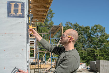 Full-frame view of an installer using the DEWALT DWHT75900 carbon fiber hammer tacker outdoors on a construction site, showcasing the tool's durability in professional environments.