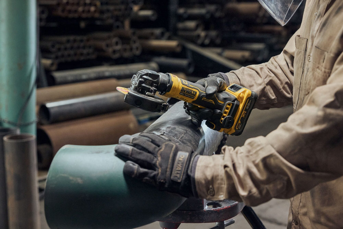 Close-up action view of a structural metalworker wearing thick leather safety gloves using the DEWALT 4 inch cordless angle grinder to prepare and grind a curved steel pipe elbow piece