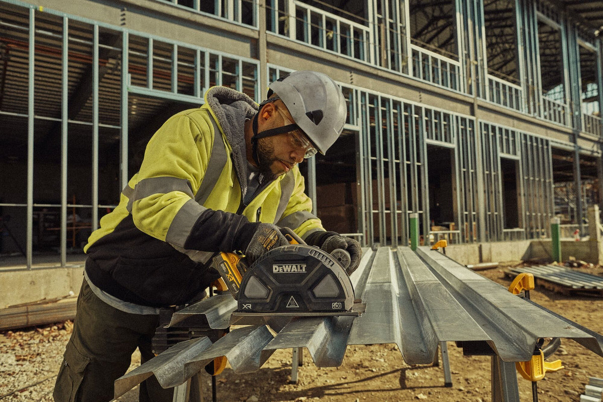 Construction site action shot of a commercial contractor wearing a hard hat and safety glasses using the DEWALT DCS383H1 cordless circular saw to cut corrugated steel roof decking sheets on sawhorses