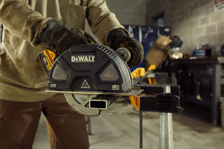 Close-up field photograph of a metal fabricator wearing protective gloves operating the DEWALT 7.25 inch cordless metal cutting saw to slice through steel box tubing with sparks flying in a fabrication shop