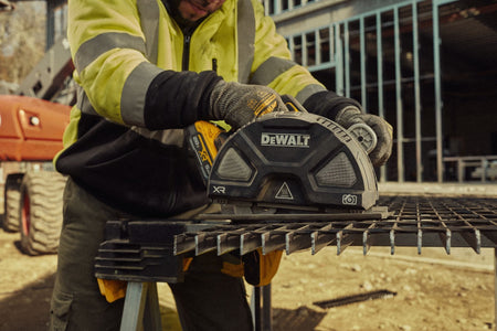 On-site building construction photograph of a worker in a high-visibility safety jacket utilizing the DEWALT 20V MAX XR brushless circular saw to precisely cut structural metal framing studs on a workbench