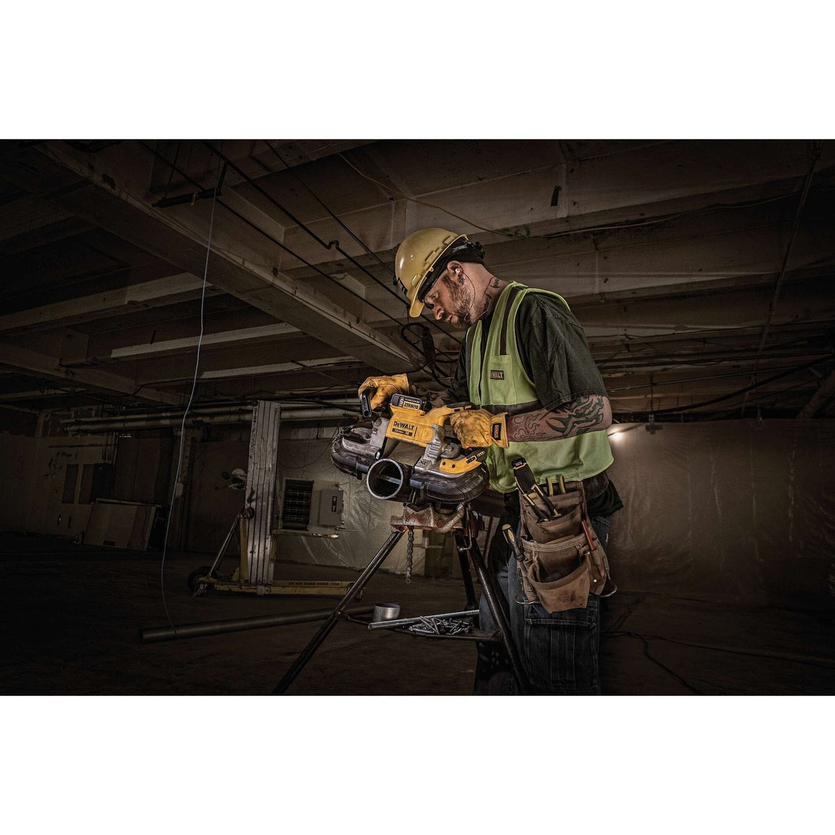 Construction trade professional wearing a hard hat, safety glasses, and high-visibility vest operating the DEWALT DCS374P2 cordless portable bandsaw to slice a thick metal conduit secured on a pipe tristan vise stand