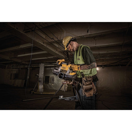 Construction trade professional wearing a hard hat, safety glasses, and high-visibility vest operating the DEWALT DCS374P2 cordless portable bandsaw to slice a thick metal conduit secured on a pipe tristan vise stand