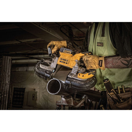 Close up industrial action view of a mechanical worker wearing heavy duty leather gloves while using the DEWALT DCS374P2 deep cut bandsaw to section structural iron piping on a workshop floor