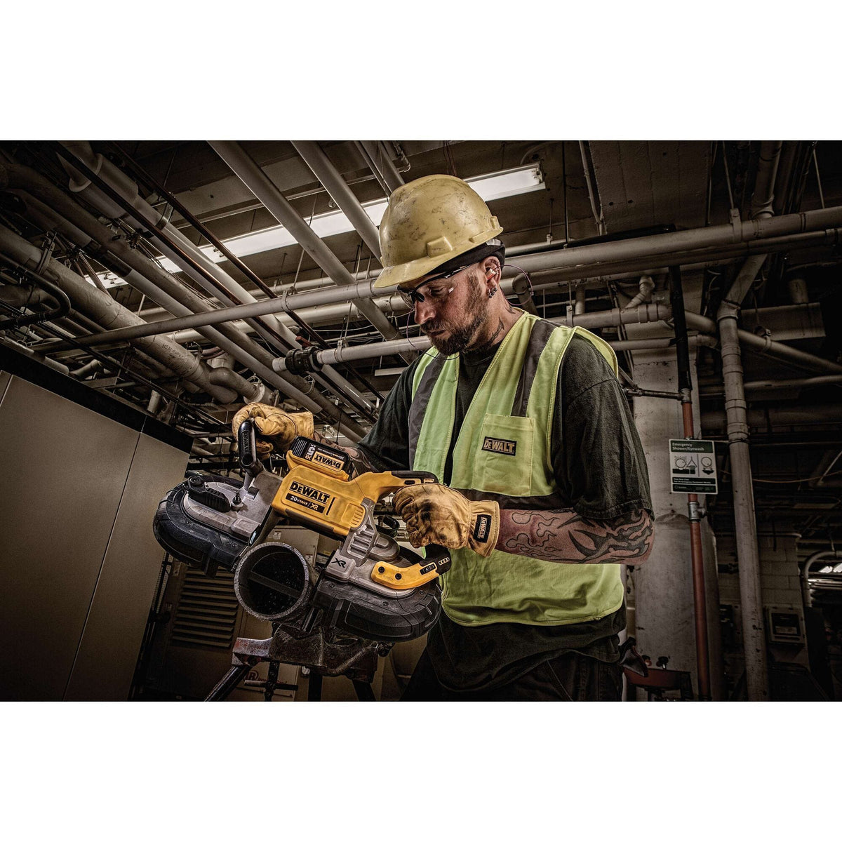 Low angle portrait shot of an electrician wearing protective safety equipment operating the DEWALT 20V MAX XR brushless portable bandsaw beneath exposed overhead industrial piping grids