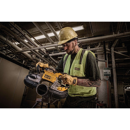 Low angle portrait shot of an electrician wearing protective safety equipment operating the DEWALT 20V MAX XR brushless portable bandsaw beneath exposed overhead industrial piping grids