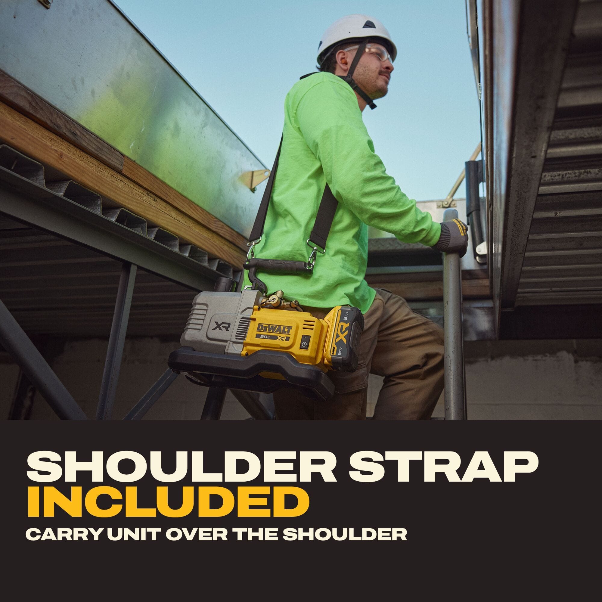 HVAC technician in a high-visibility green shirt and hard hat carrying the DEWALT cordless vacuum pump using the included shoulder strap while ascending an outdoor industrial metal staircase to a rooftop jobsite.
