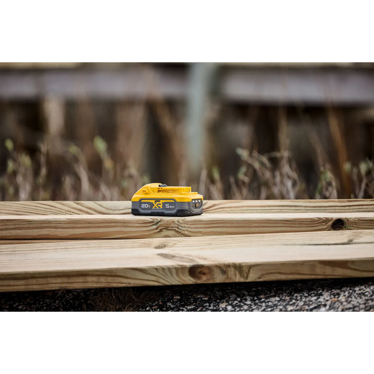 A lifestyle shot of the DEWALT 20V MAX POWERSTACK 5Ah battery pack resting on a wooden construction plank. The image showcases the battery's rugged design and compact footprint in a real-world jobsite environment, highlighting its professional-grade durability.