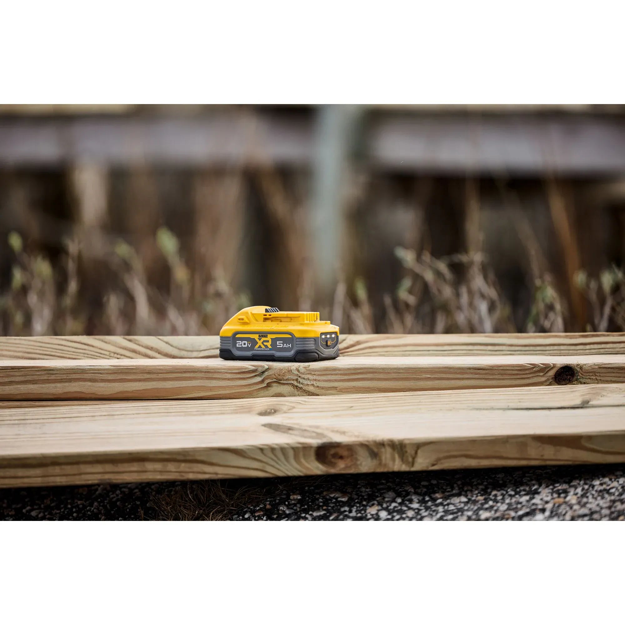 A lifestyle shot of the DEWALT 20V MAX POWERSTACK 5Ah battery pack resting on a wooden construction plank. The image showcases the battery's rugged design and compact footprint in a real-world jobsite environment, highlighting its professional-grade durability.