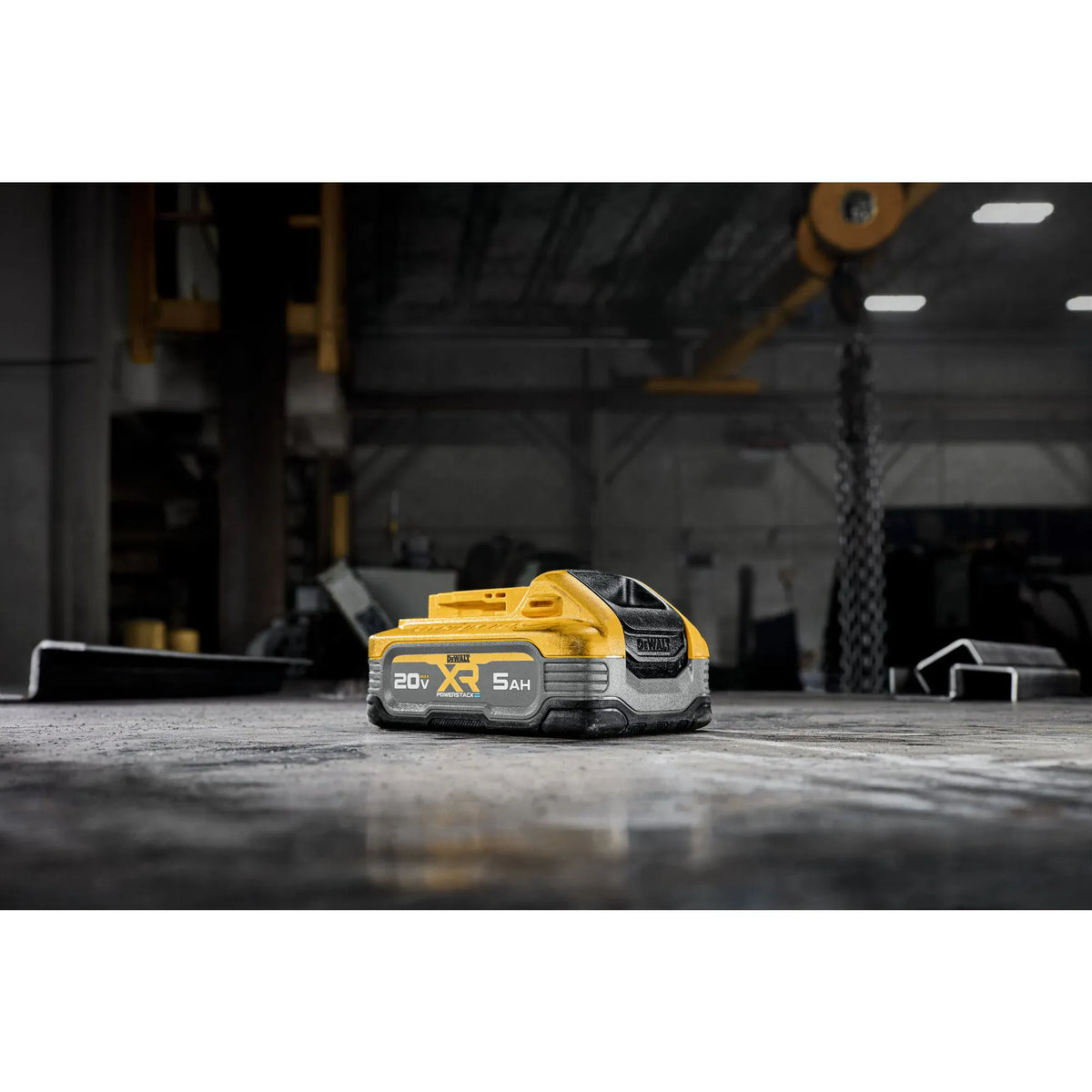 A lifestyle shot of the DEWALT 20V MAX POWERSTACK 5Ah battery pack resting on a concrete floor in a workshop setting. The image highlights the battery's compact footprint and rugged design in a professional industrial environment.