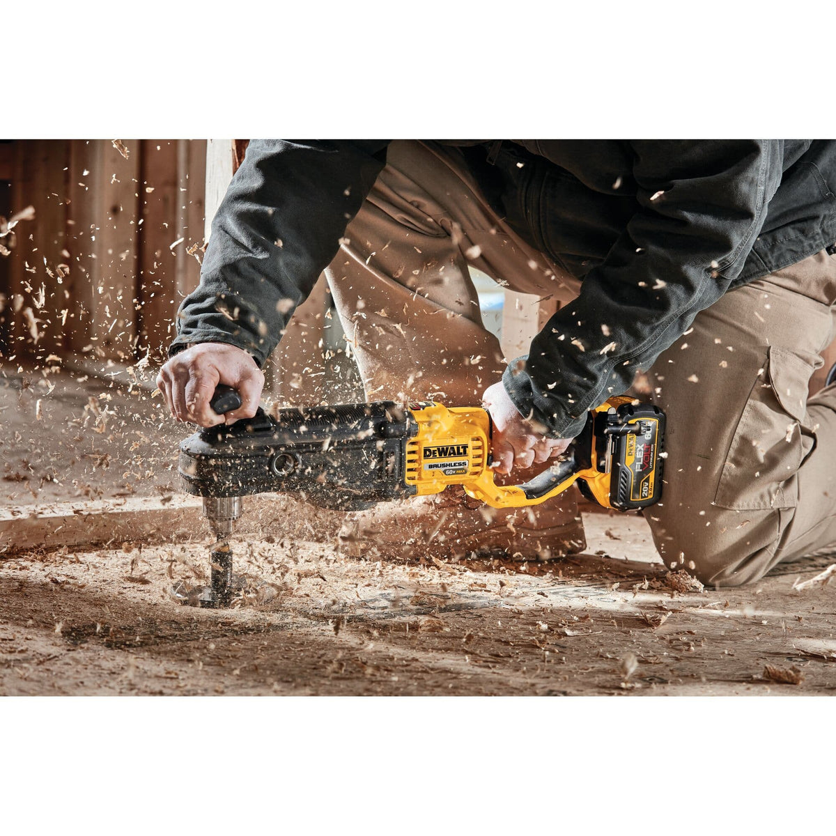 Professional worker kneeling on a wooden subfloor using the DEWALT 60V MAX cordless in-line stud and joist drill with a large self-feed bit to bore heavy-duty holes, with wood chips actively flying.